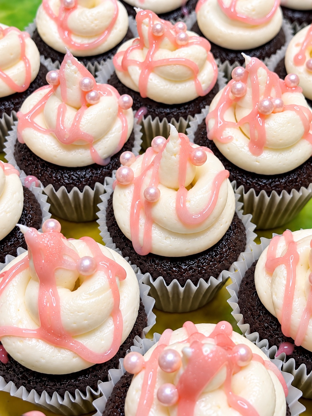 Close-up of chocolate mini cupcakes with white frosting and pink drizzle